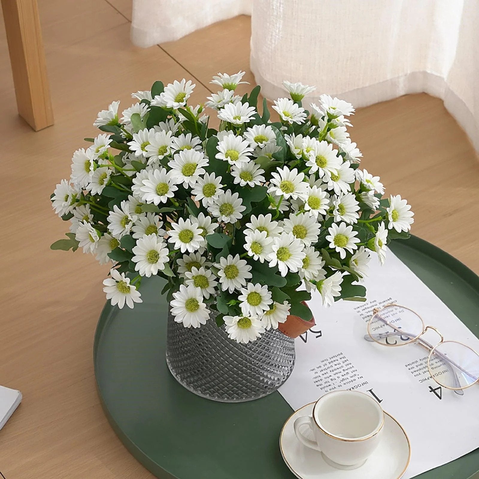 Bouquet of white flowers in a clear vase on a green tray with a cup and saucer.