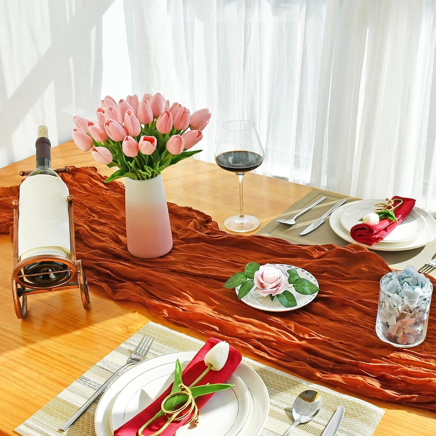 Dining table set with a red runner, pink tulips, wine glasses, and place settings.