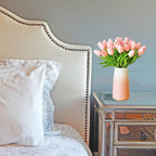 Bedroom with a bed, headboard, and a vase of pink tulips on a nightstand.