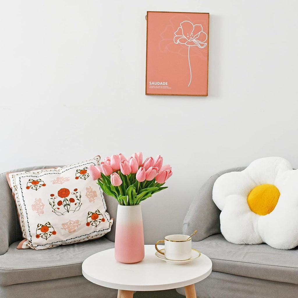 Living room with a gray sofa, decorative pillows, a vase of pink tulips, and a coffee cup.