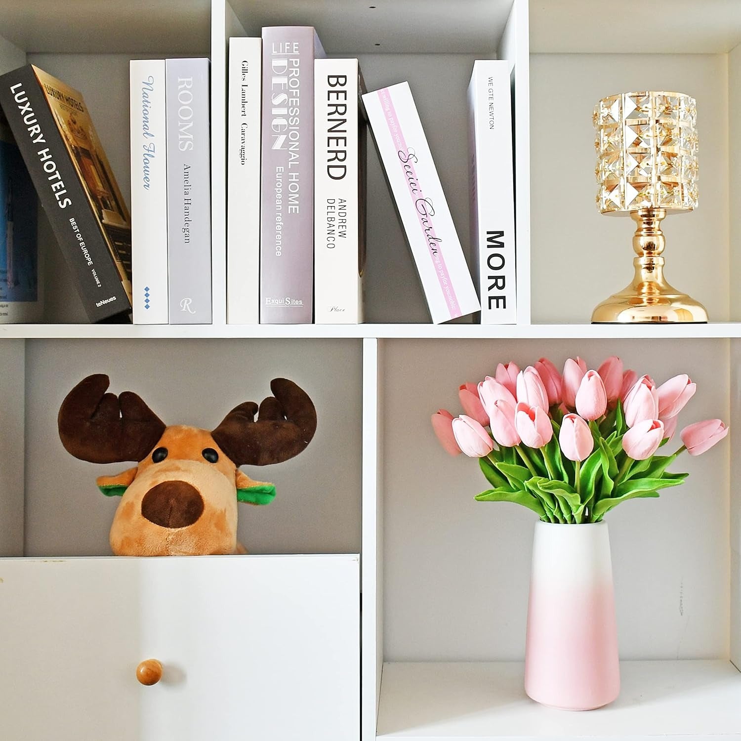 Bookshelf with books, decorative lamp, plush moose, and pink tulips in a vase.