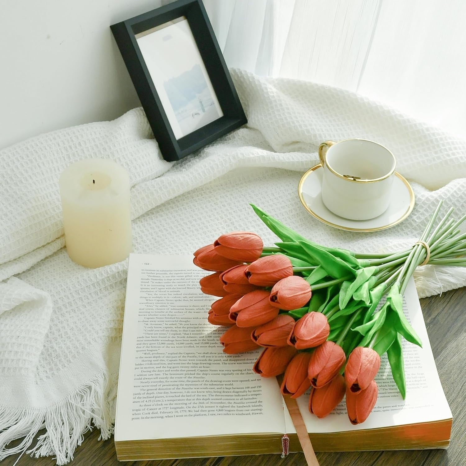 Bouquet of red tulips on an open book with a cup and candle in the background