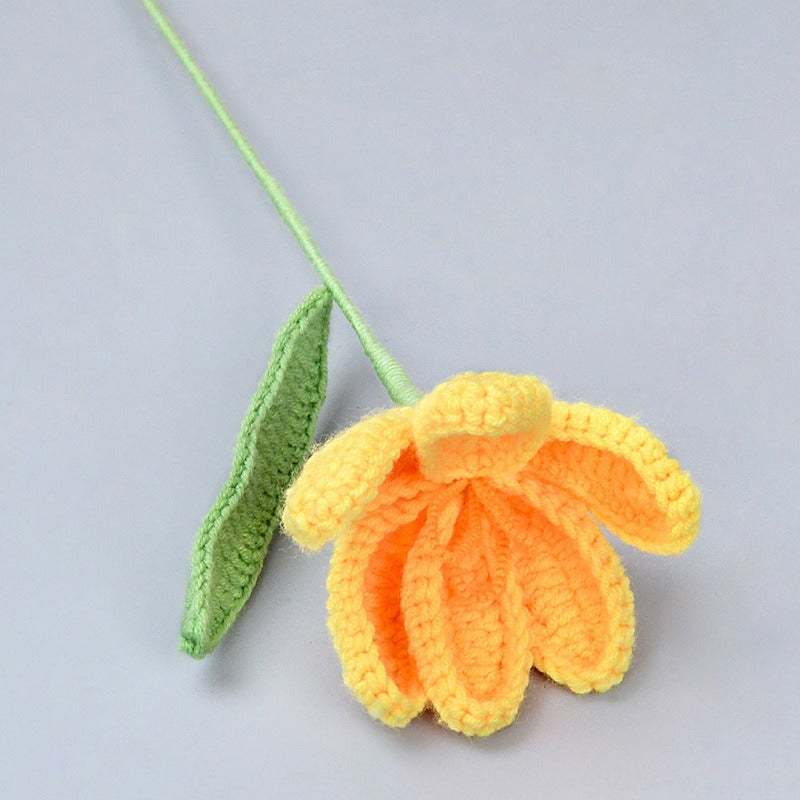 Crocheted yellow flower and green leaf on a light gray background