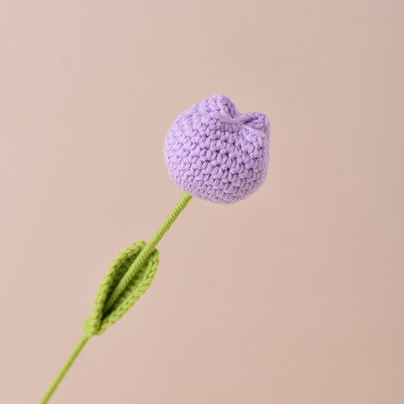 Crocheted purple flower with green stem on a beige background