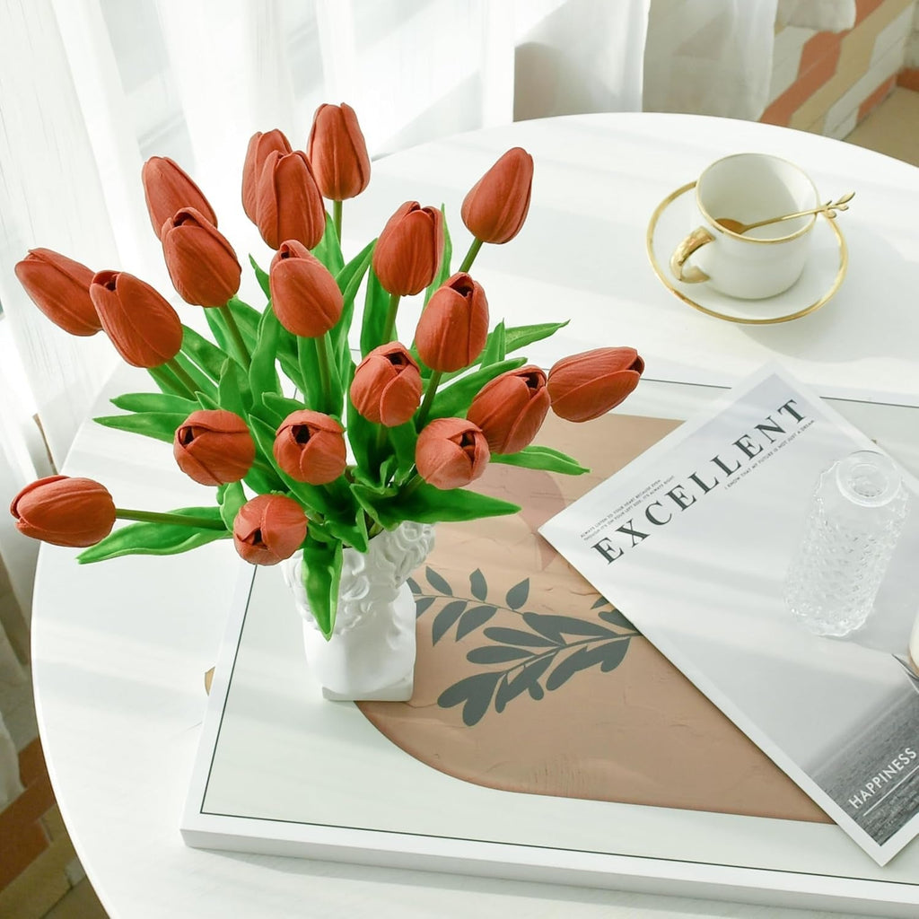 Bouquet of red tulips in a white vase on a table with a newspaper and cup.