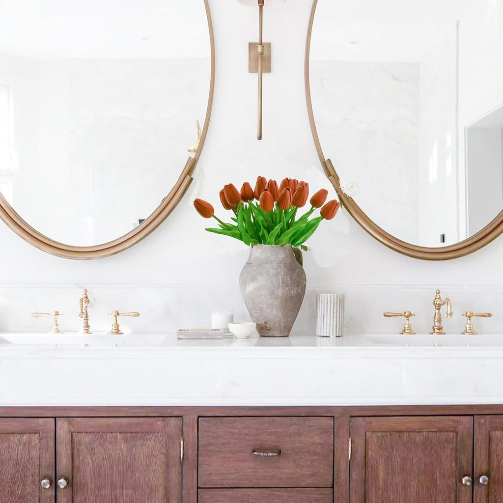 Bathroom vanity with wooden cabinets, white countertop, and gold fixtures with a vase of red tulips.