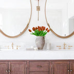 Bathroom vanity with wooden cabinets, white countertop, and gold fixtures with a vase of red tulips.