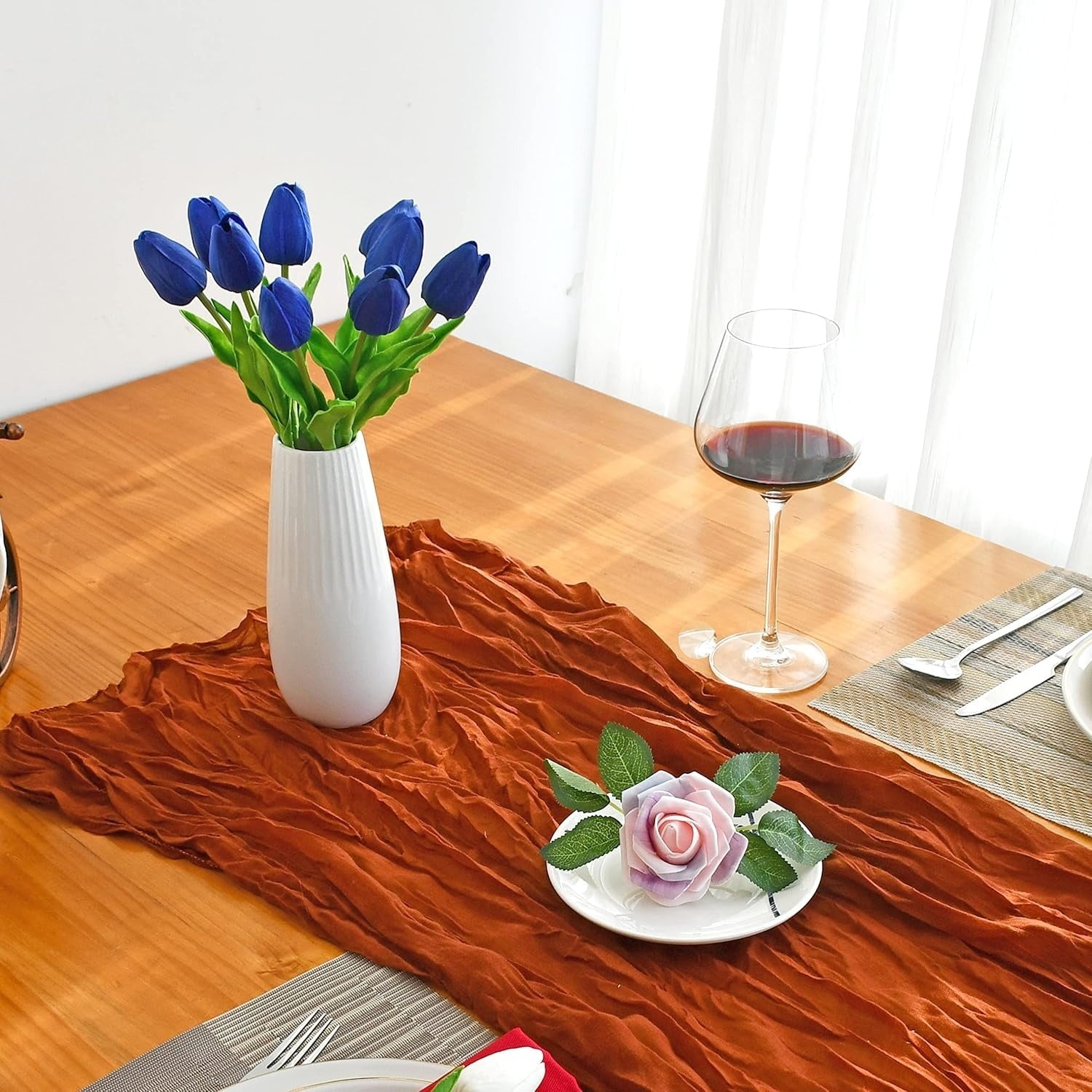Dining table setting with blue tulips in a white vase, a glass of red wine, and a small plate with a pink rose.