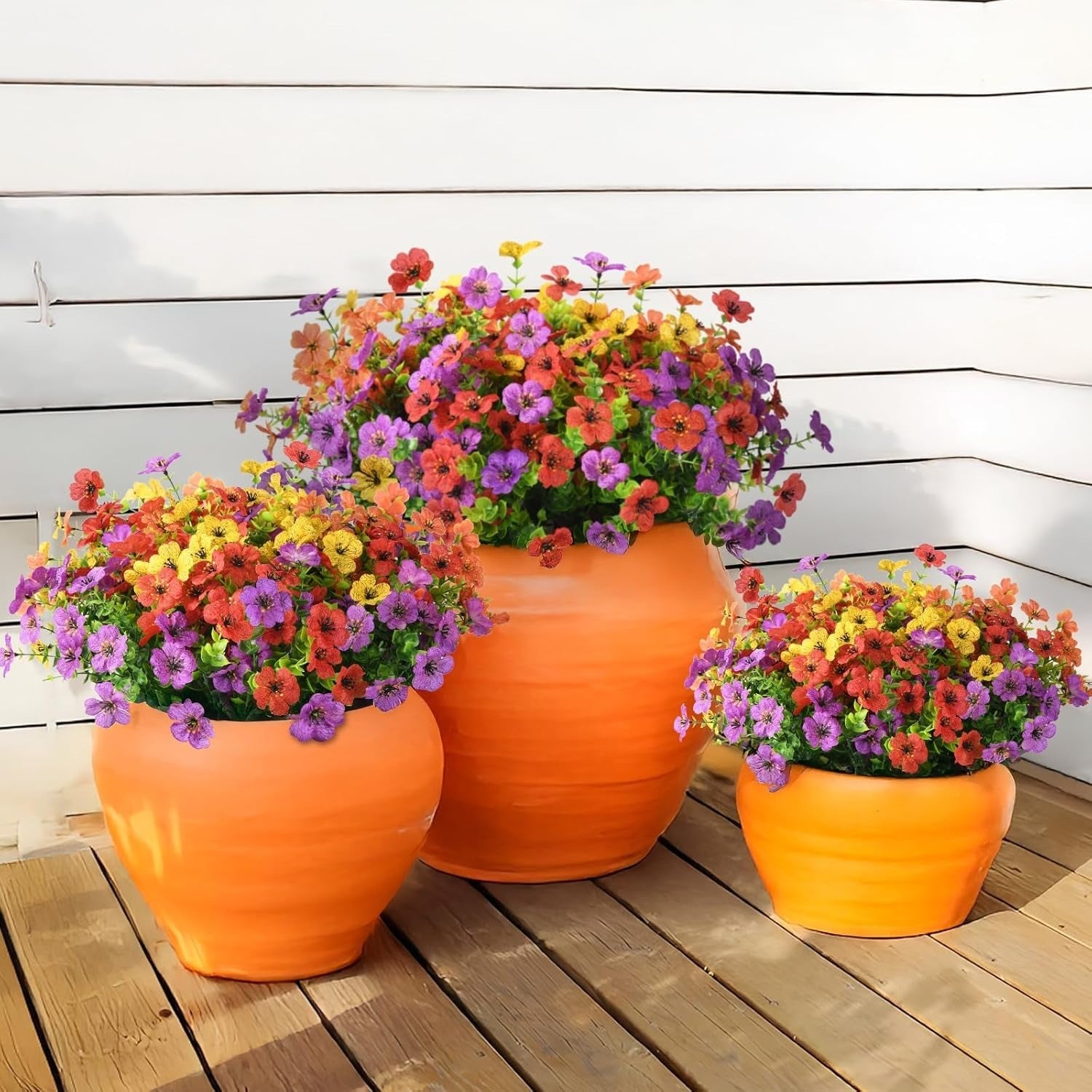 Three orange planters filled with colorful flowers on a wooden deck.