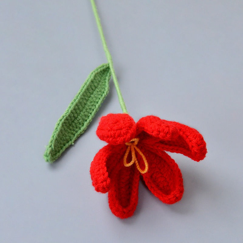 Crocheted red flower with a green stem on a gray background