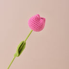 Crocheted pink tulip with green stem and leaf on a beige background