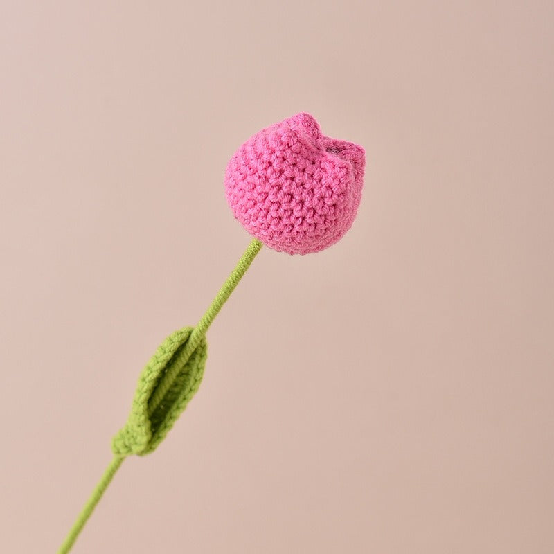 Crocheted pink tulip with green stem and leaf on a beige background