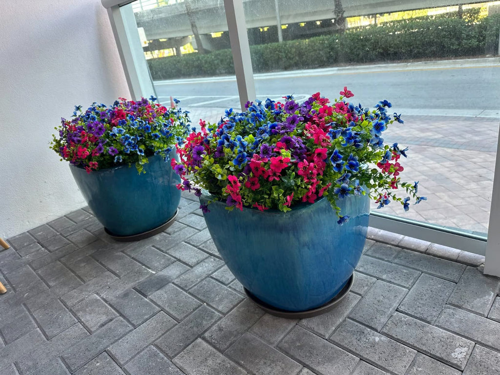Two blue pots with colorful flowers on a paved area.