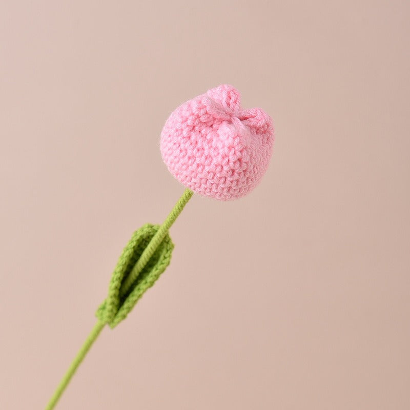 Knitted pink flower with green stem on a beige background