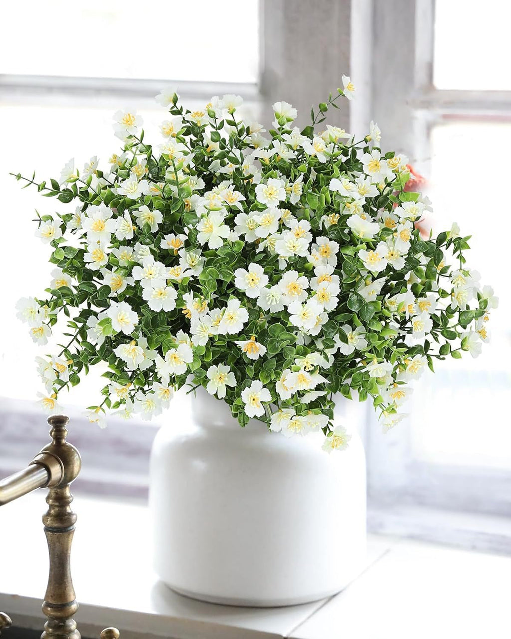 White vase with artificial flowers on a windowsill
