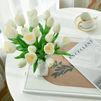 Bouquet of white tulips in a vase on a table with a magazine and cup.