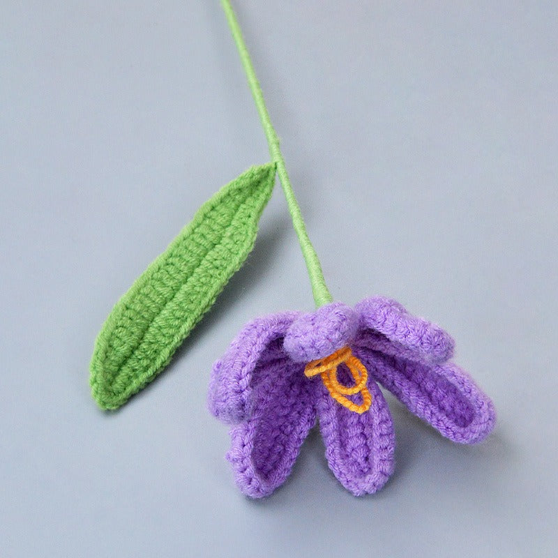 Crocheted purple flower with green leaf on a gray background