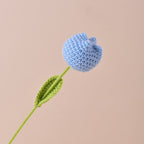 Crocheted blue flower with a green stem on a beige background