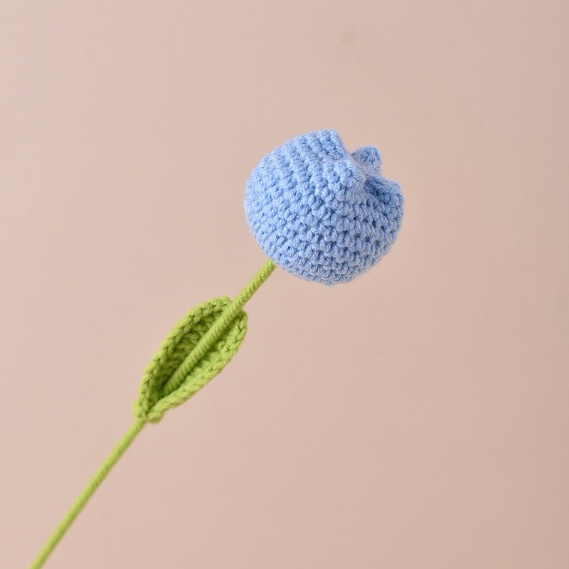 Crocheted blue flower with a green stem on a beige background