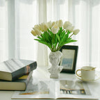 Decorative setup with white tulips in a vase, books, and a cup on a table.