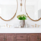 Bathroom vanity with wooden cabinets, white countertop, and gold fixtures.