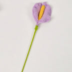 Crocheted flower with purple petals and yellow center on a white background