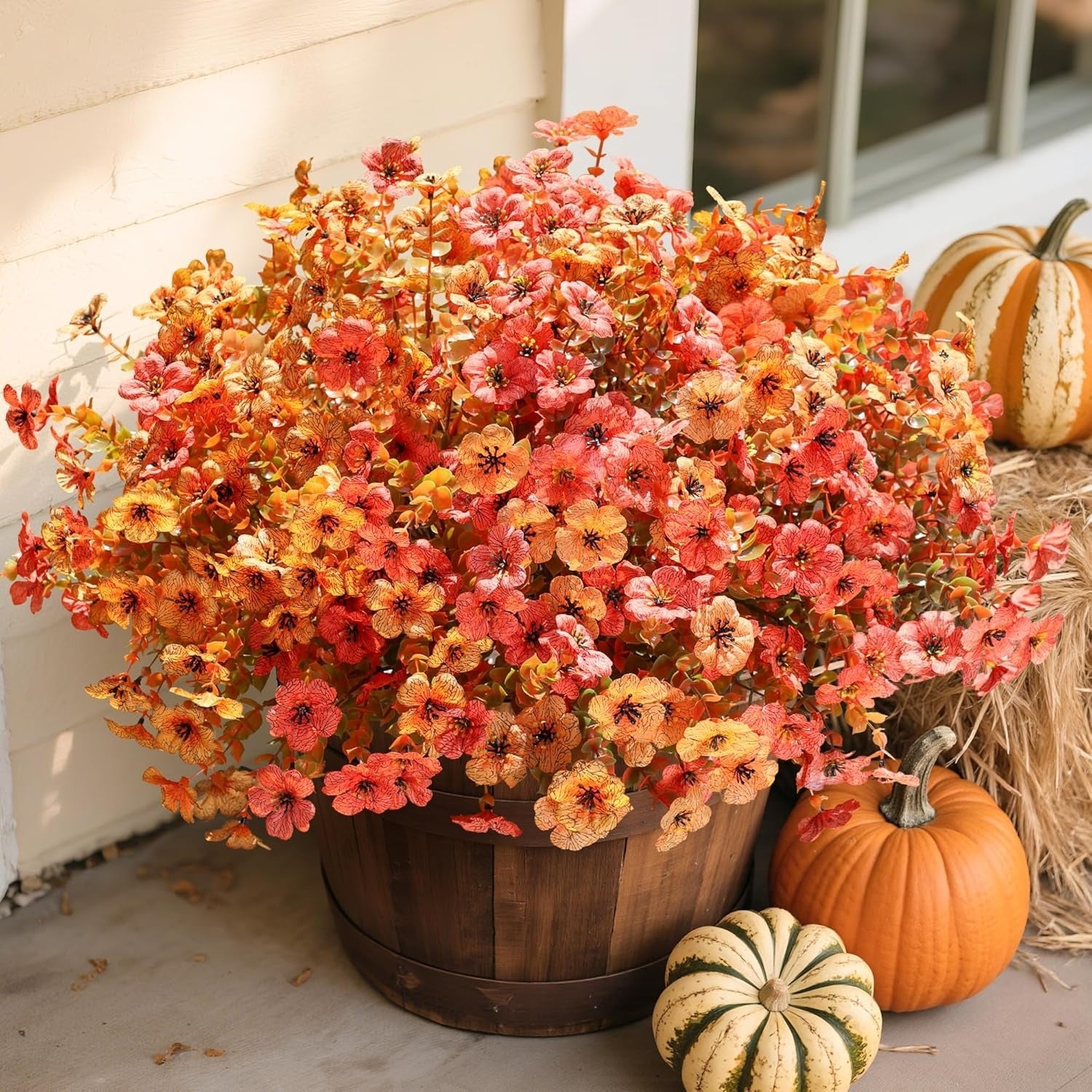 Autumn-themed floral arrangement in a wooden barrel with pumpkins on a porch.