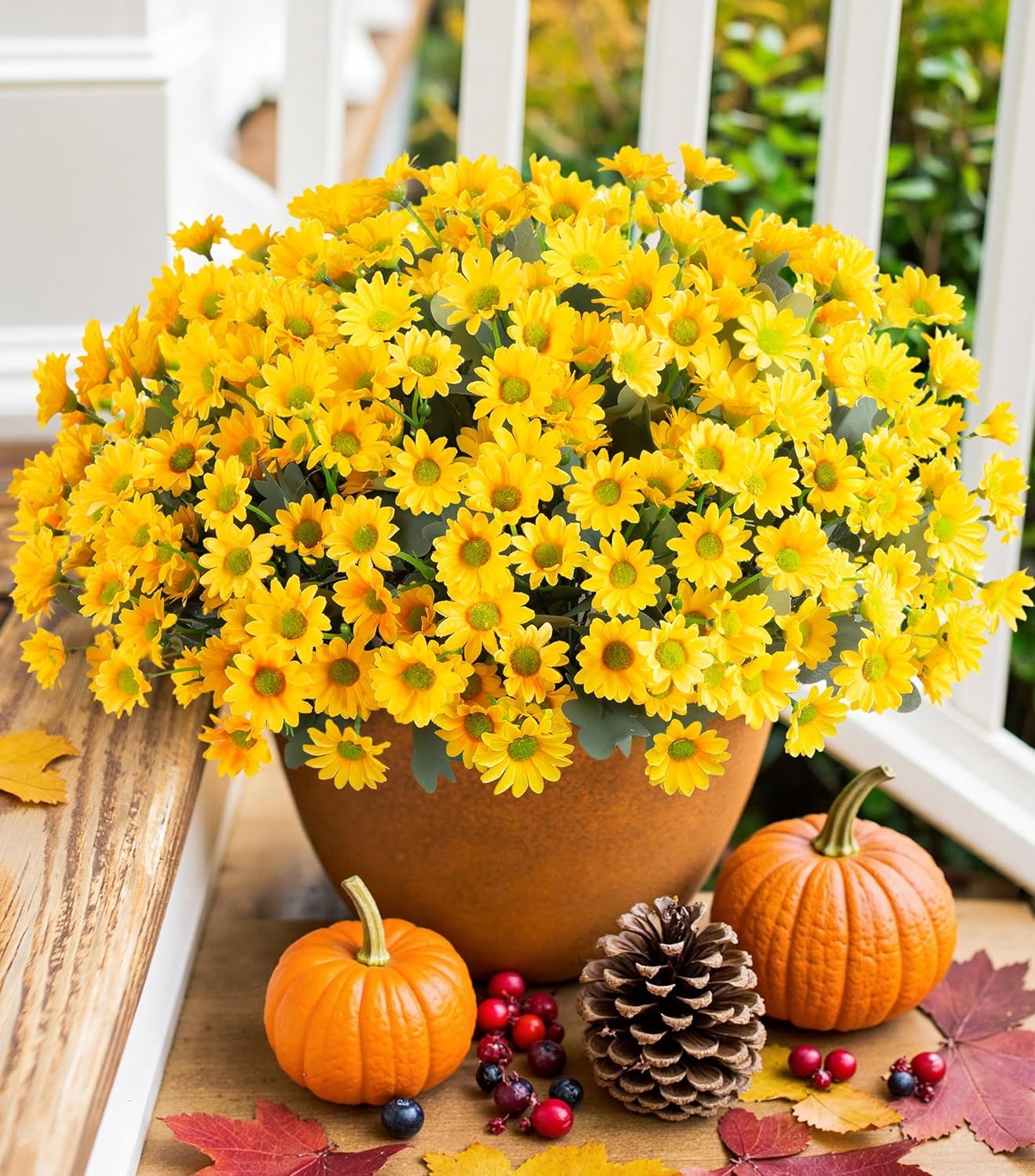 Potted plant with yellow flowers on a wooden surface with pumpkins and berries.