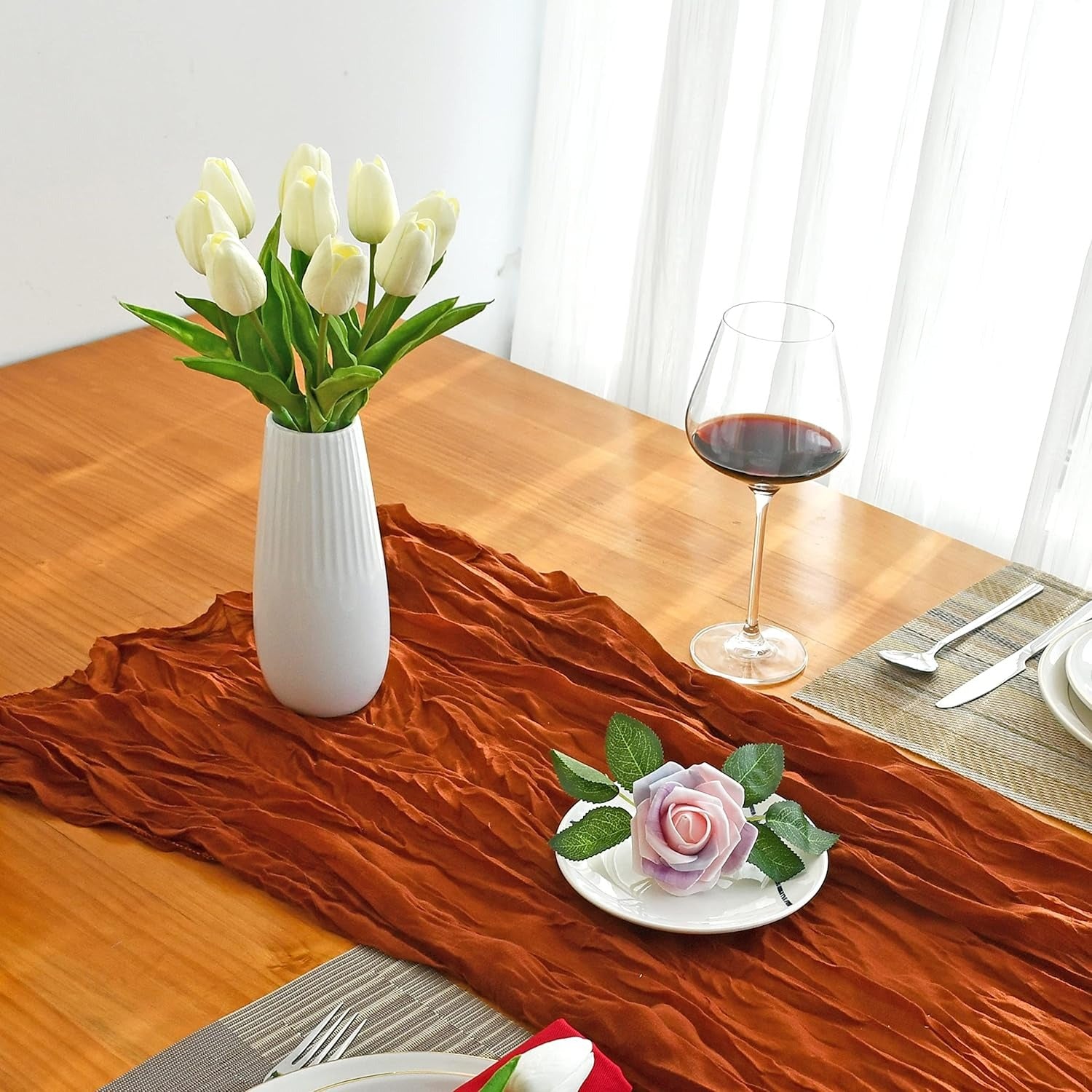 Dining table set with a vase of white tulips, a glass of red wine, and a small dish with a pink rose.