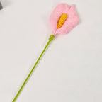 Crocheted pink flower with a green stem on a light gray background
