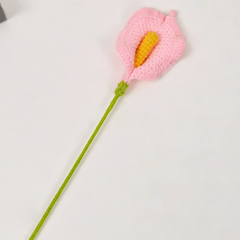 Crocheted pink flower with a green stem on a light gray background
