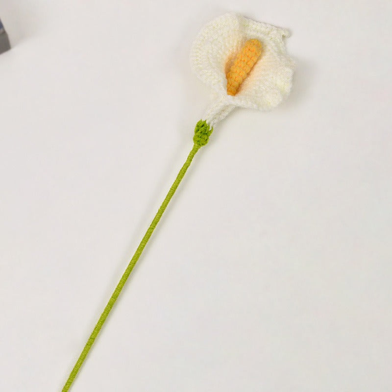Knitted flower with white petals and a green stem on a light gray background
