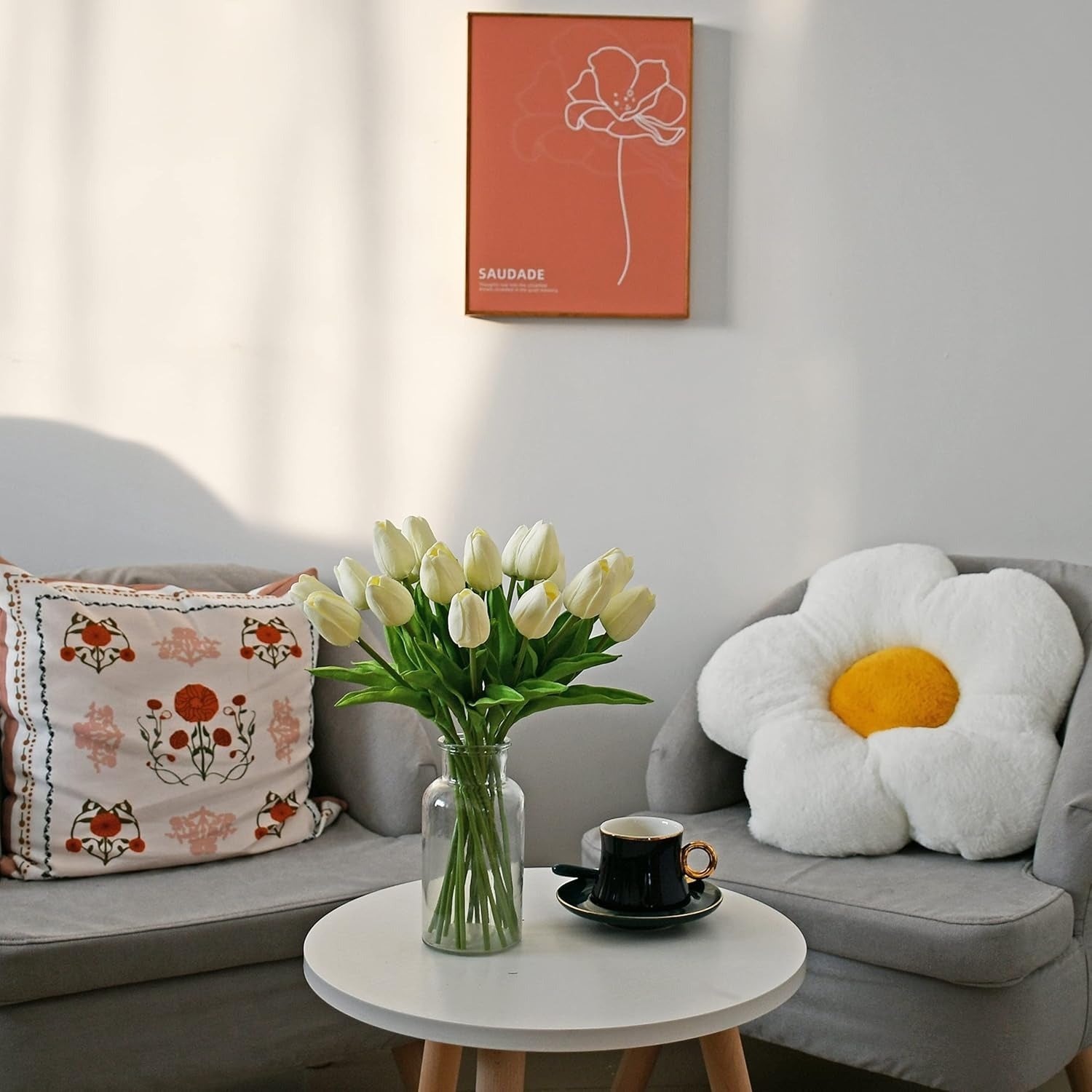 Living room with a gray sofa, floral pillow, and a vase of white tulips on a small round table.