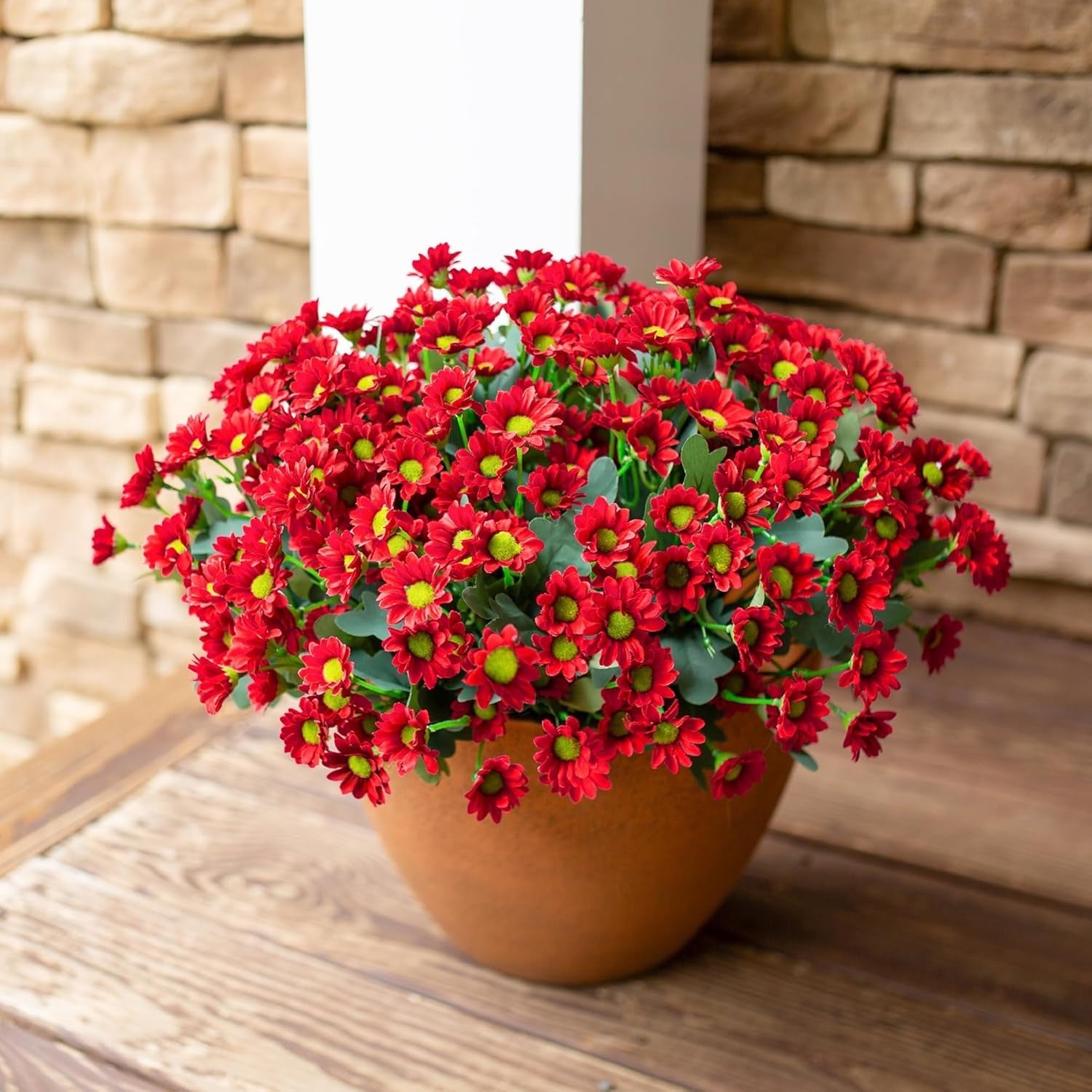 Potted red flowers on a wooden surface with a stone wall background