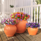 Three orange ceramic pots with colorful flowers on a wooden deck.