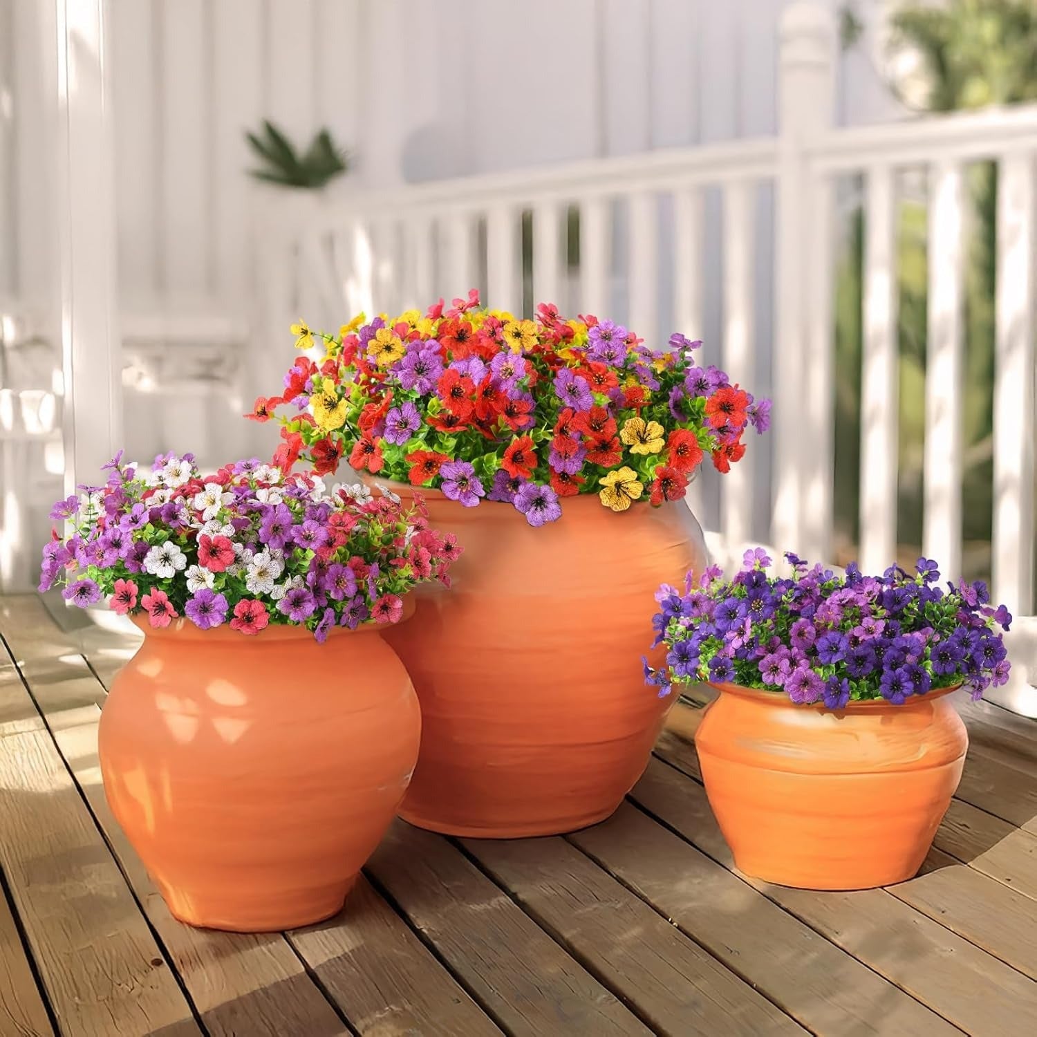 Three orange ceramic pots with colorful flowers on a wooden deck.