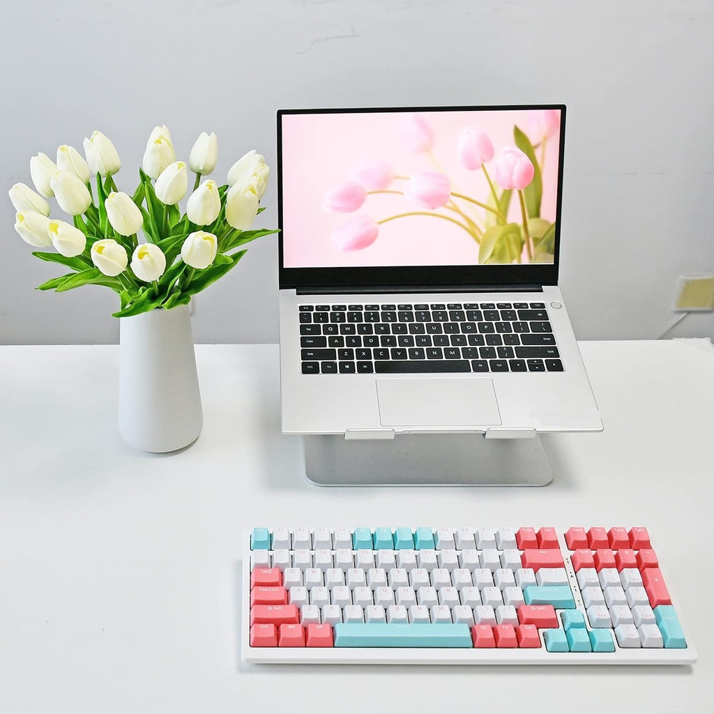 Laptop on a stand with a colorful keyboard on a desk, next to a vase of tulips.