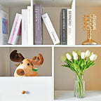 Shelving unit with books, a stuffed moose toy, and a vase of white tulips.