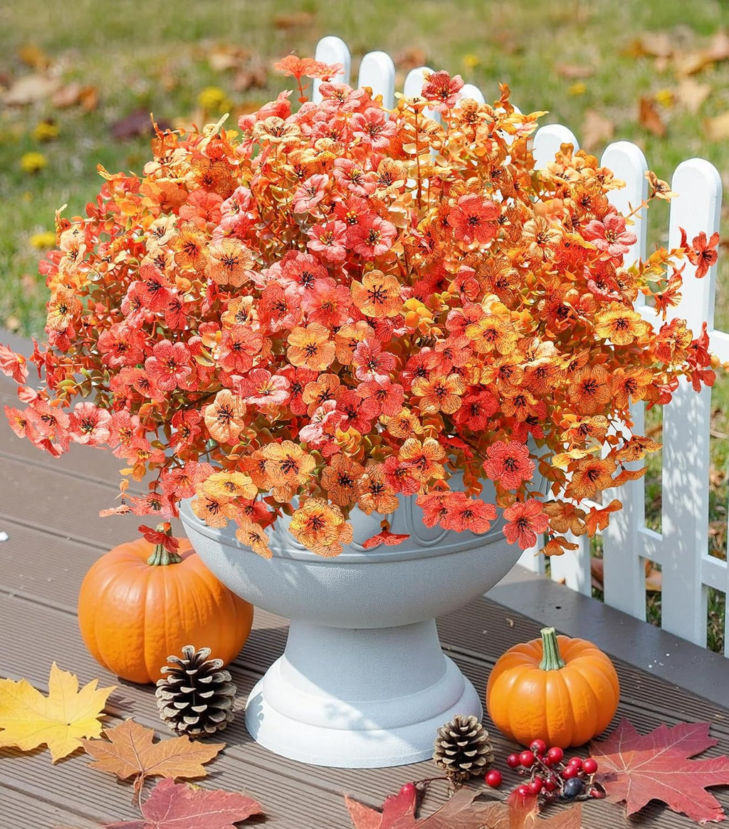 Decorative arrangement of autumn flowers in a white vase on a wooden surface with pumpkins and pinecones.
