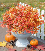 Decorative arrangement of autumn flowers in a white vase on a wooden surface with pumpkins and pinecones.