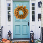 Turquoise front door with a wreath and pumpkins on a porch