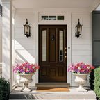 Front door of a house with flower pots on either side, featuring a doormat.
