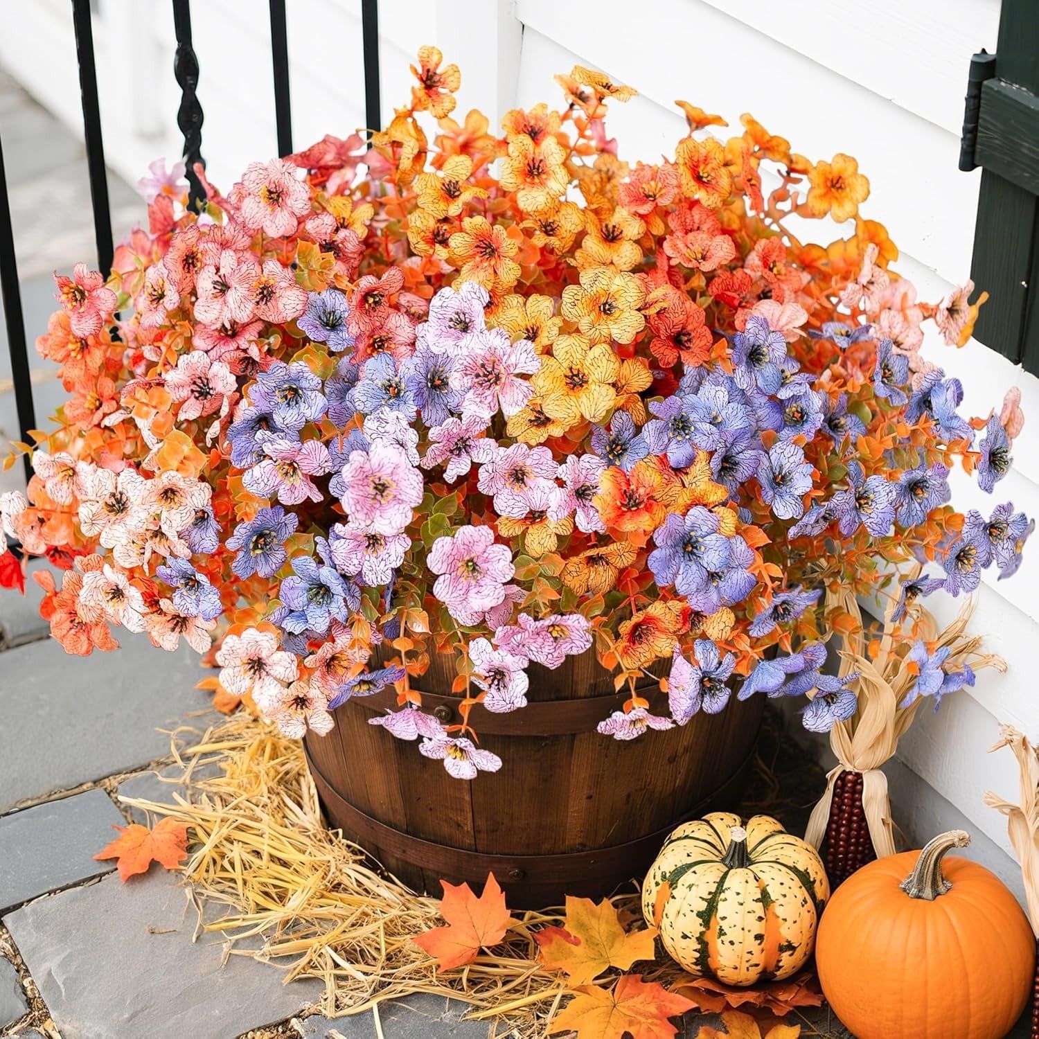 Decorative arrangement of flowers in a wooden barrel with pumpkins and leaves on a stone surface.