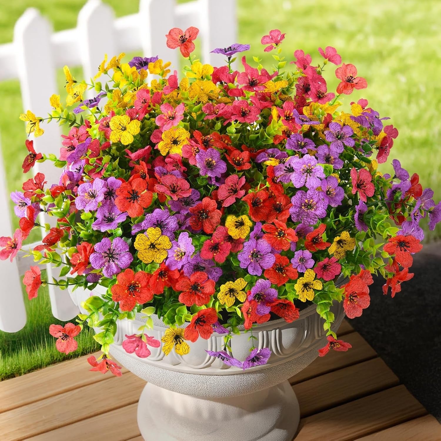 Colorful flowers in a white urn on a wooden deck with a blurred background