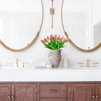 Bathroom vanity with wooden cabinets, white countertop, and pink tulips in a vase.