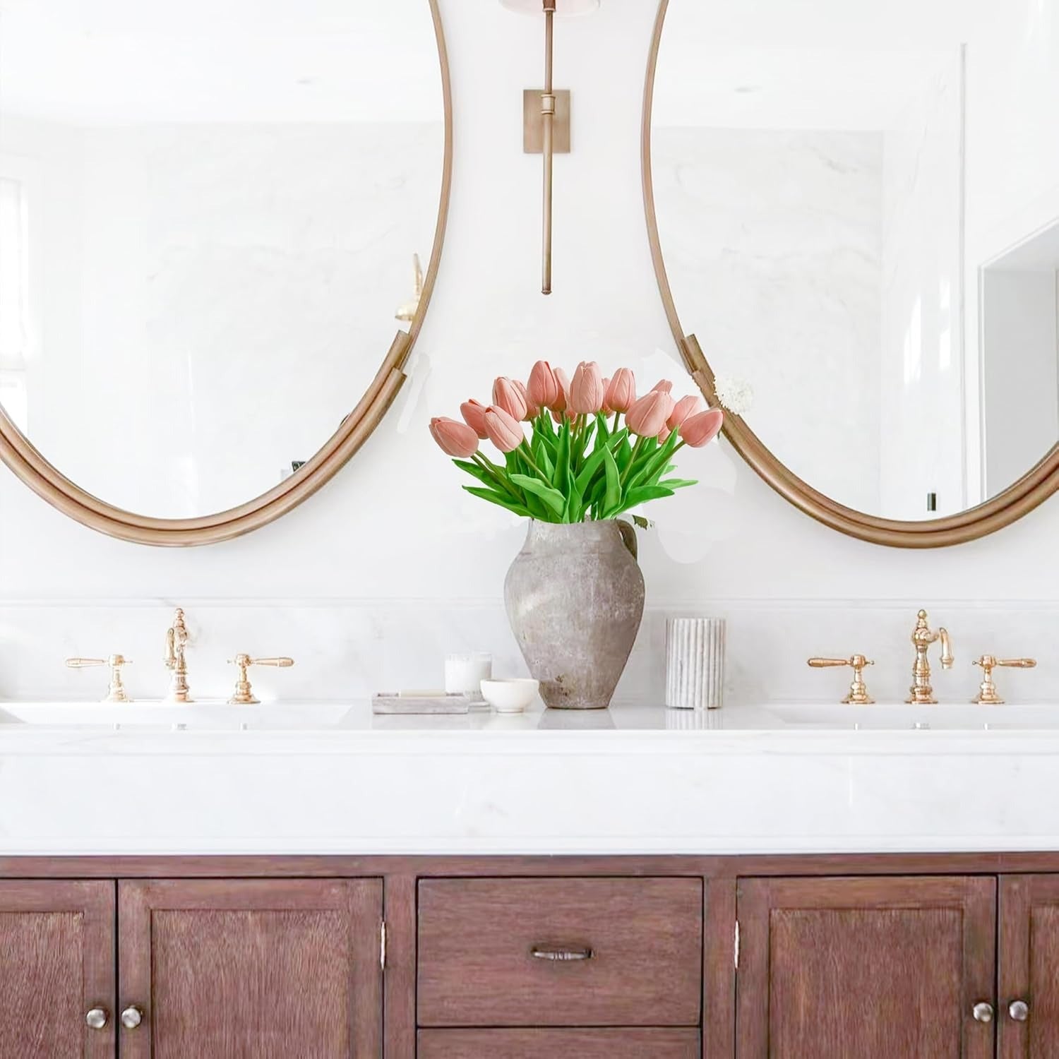 Bathroom vanity with wooden cabinets, white countertop, and pink tulips in a vase.