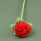 Crocheted red rose with green leaves on a gray background