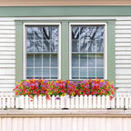 Floral window box on a white picket fence in front of a house with a window.