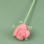 Crocheted pink flower with green leaves on a light green background