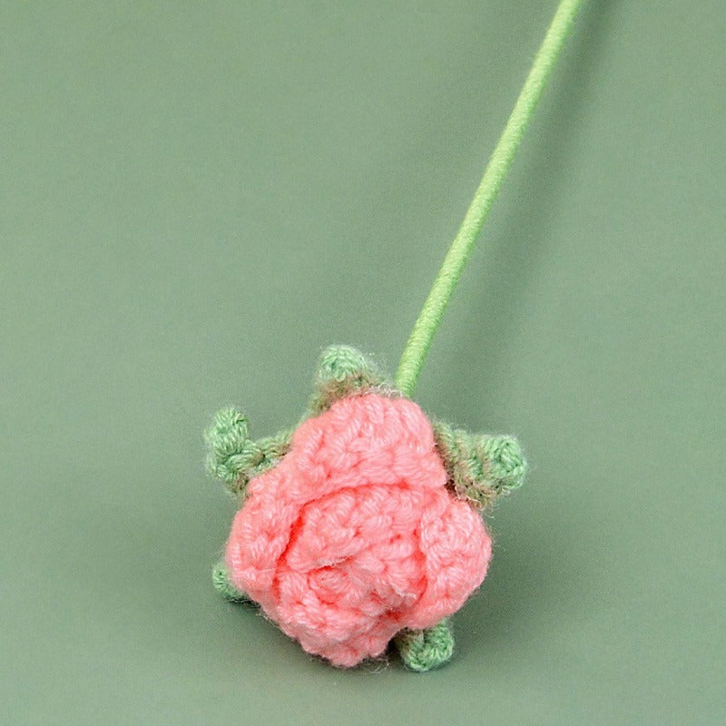 Crocheted pink flower with green leaves on a light green background